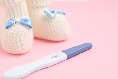 Photo of Pregnancy test and knitted booties on pink background, closeup