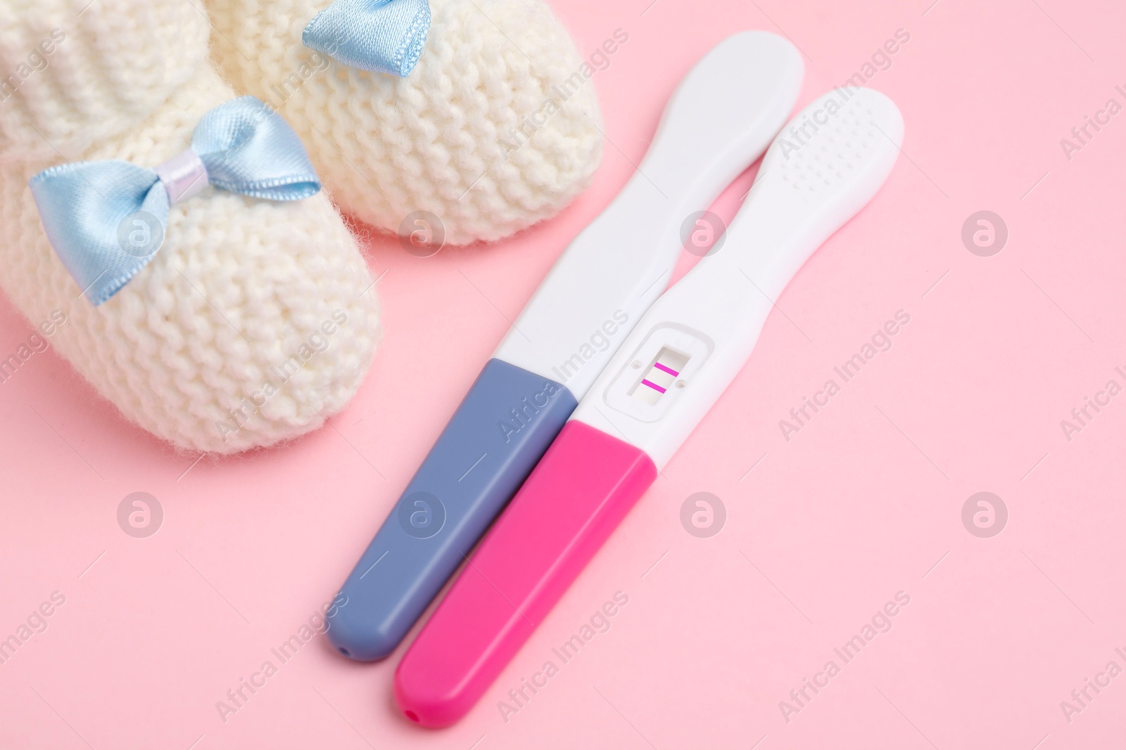 Photo of Pregnancy tests and knitted booties on pink background, closeup