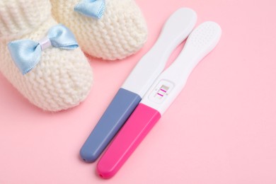 Photo of Pregnancy tests and knitted booties on pink background, closeup