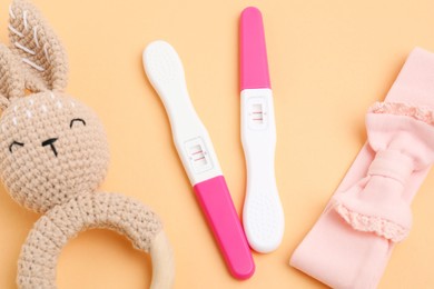 Photo of Pregnancy tests, baby rattle and headband on pale orange background, closeup