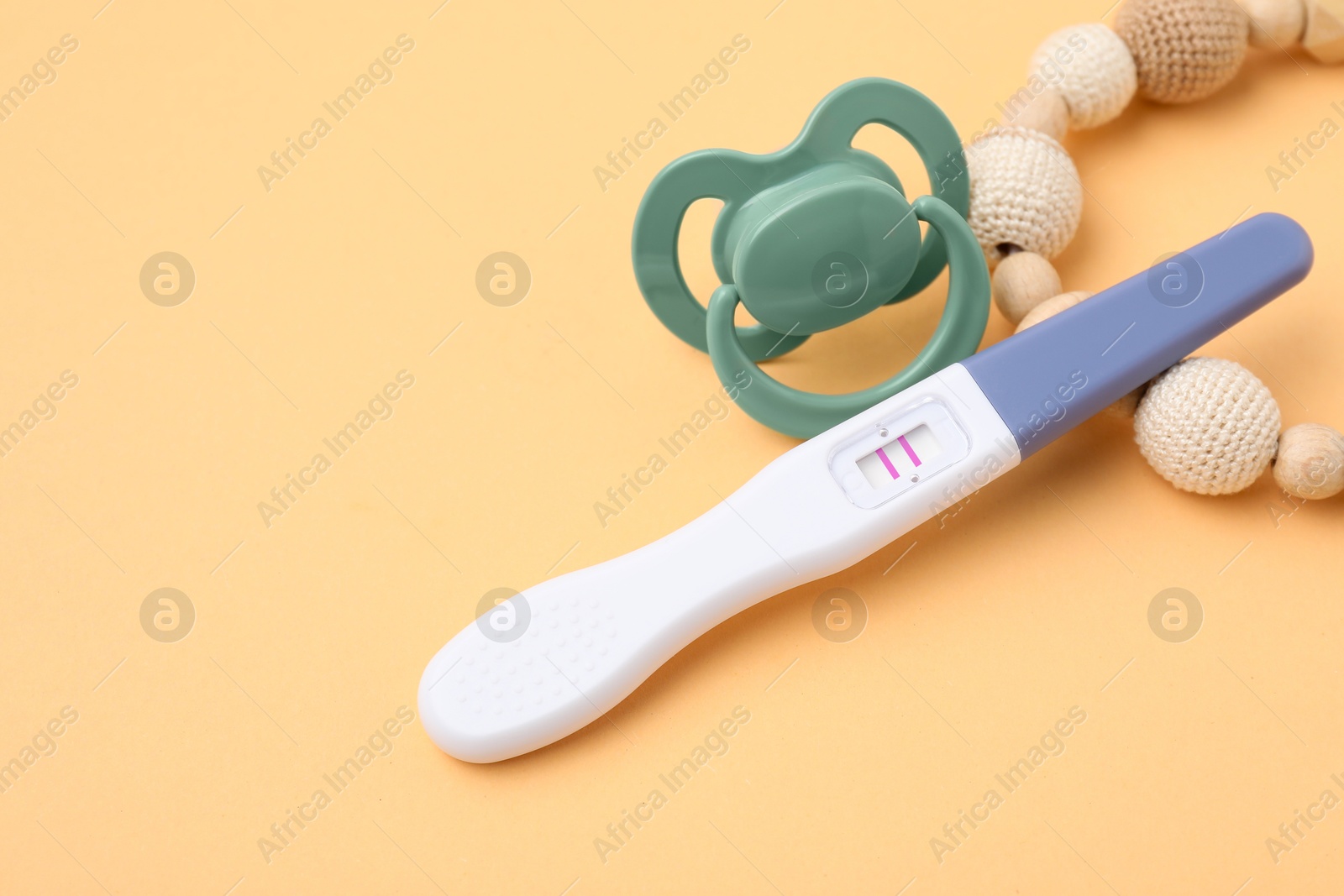 Photo of Pregnancy test, pacifier and teether on pale orange background, closeup