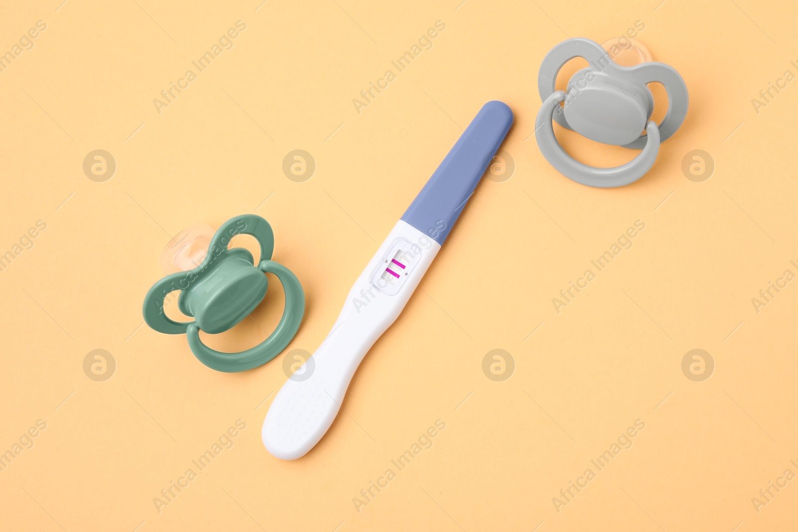 Photo of Pregnancy test and pacifiers on pale orange background