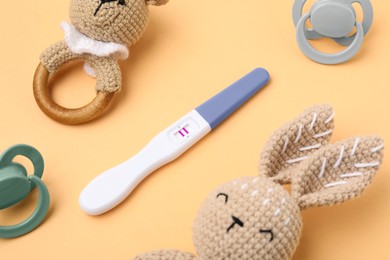 Photo of Pregnancy test, baby rattles and pacifiers on pale orange background, closeup