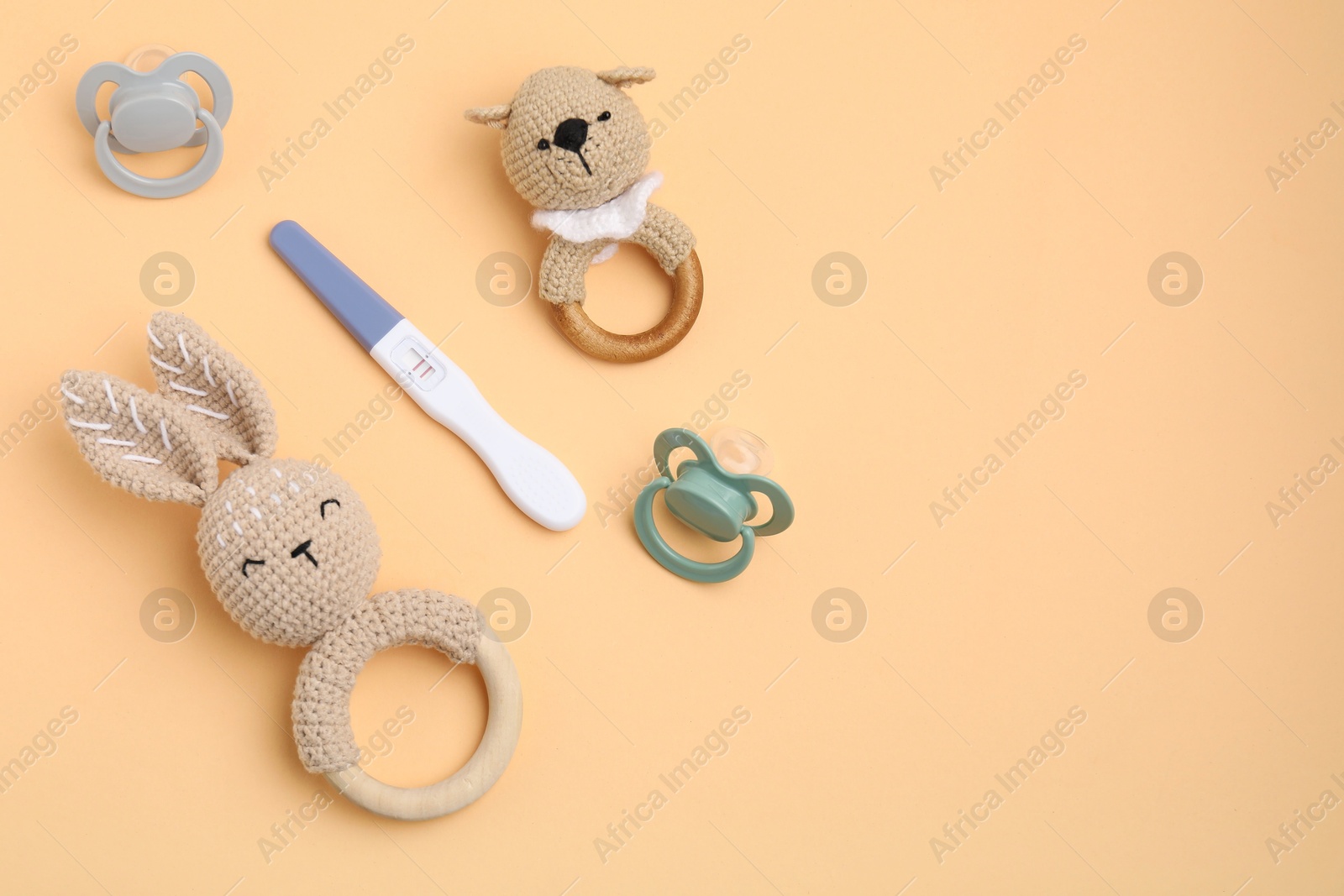 Photo of Pregnancy test, baby rattles and pacifiers on pale orange background, flat lay. Space for text