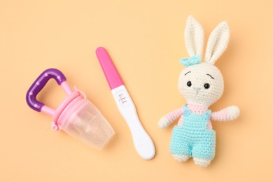 Photo of Pregnancy test, nibbler and toy bunny on pale orange background, top view