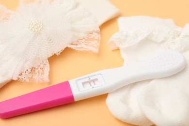 Photo of Pregnancy test, headband and socks on pale orange background, closeup