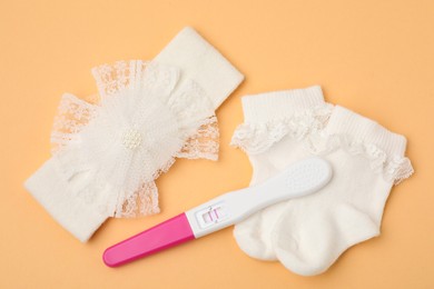 Photo of Pregnancy test, headband and socks on pale orange background, top view