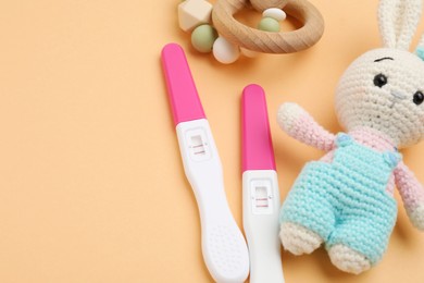 Photo of Pregnancy tests, baby rattle and toy bunny on pale orange background, closeup. Space for text