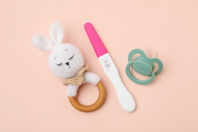 Photo of Pregnancy test, rattle and pacifier on beige background, top view