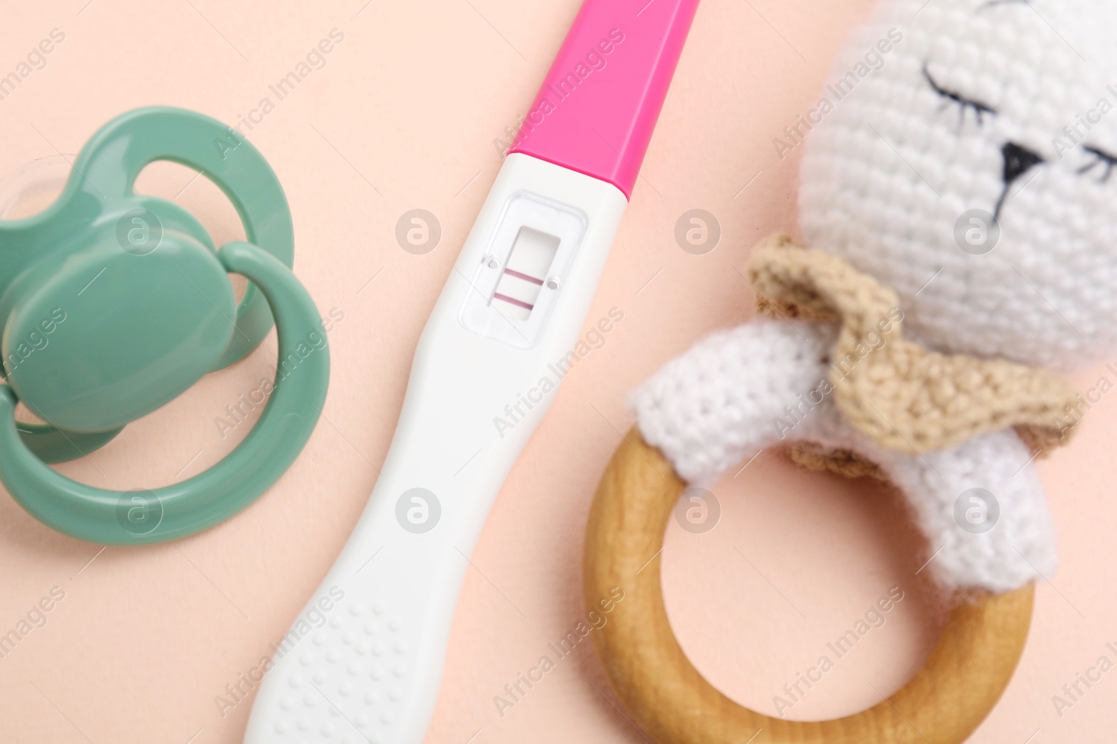 Photo of Pregnancy test, rattle and pacifier on beige background, closeup