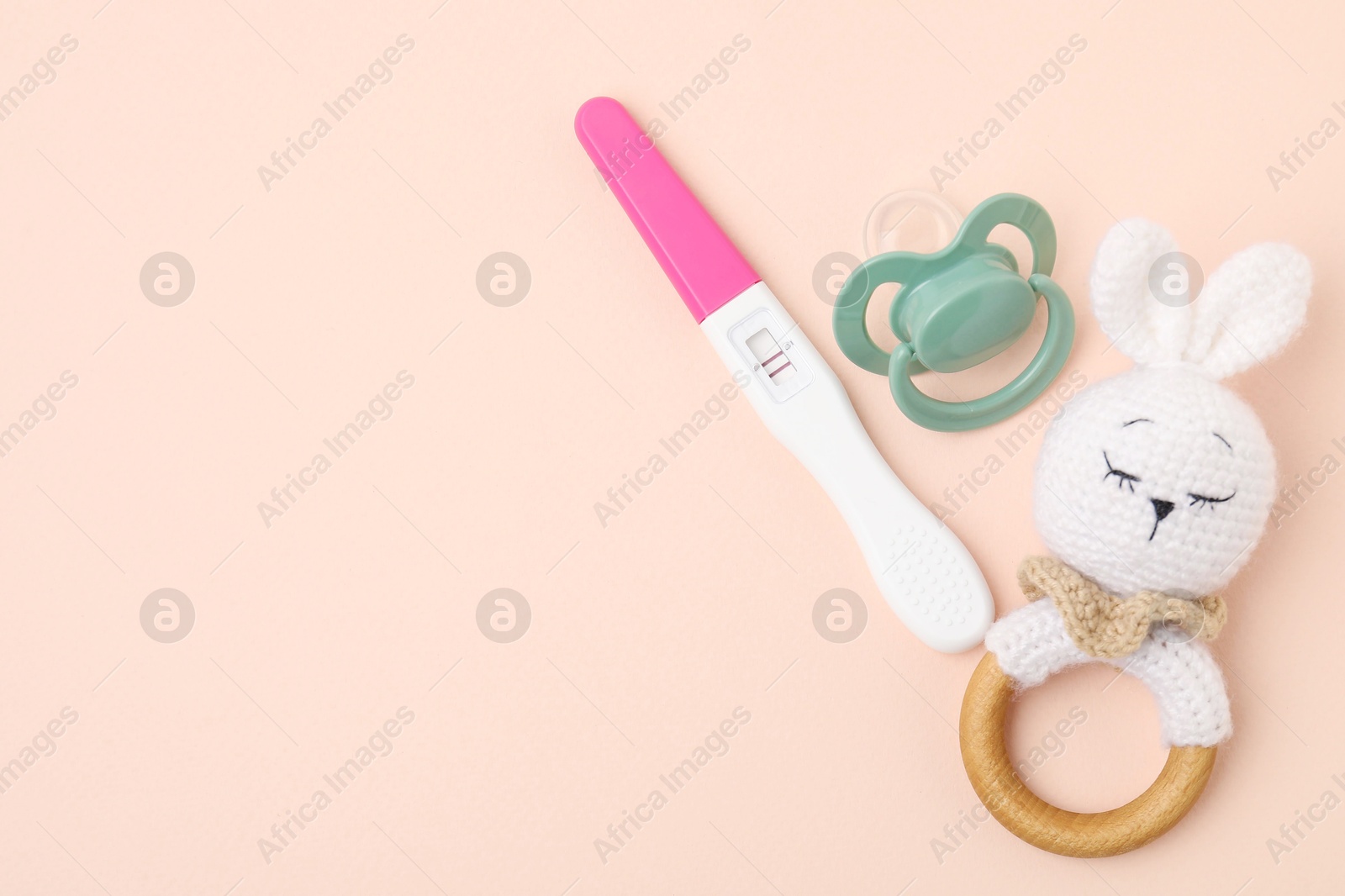 Photo of Pregnancy test, rattle and pacifier on beige background, top view. Space for text