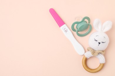 Photo of Pregnancy test, rattle and pacifier on beige background, top view. Space for text