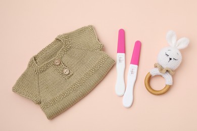 Photo of Pregnancy tests, rattle and baby clothes on beige background, top view