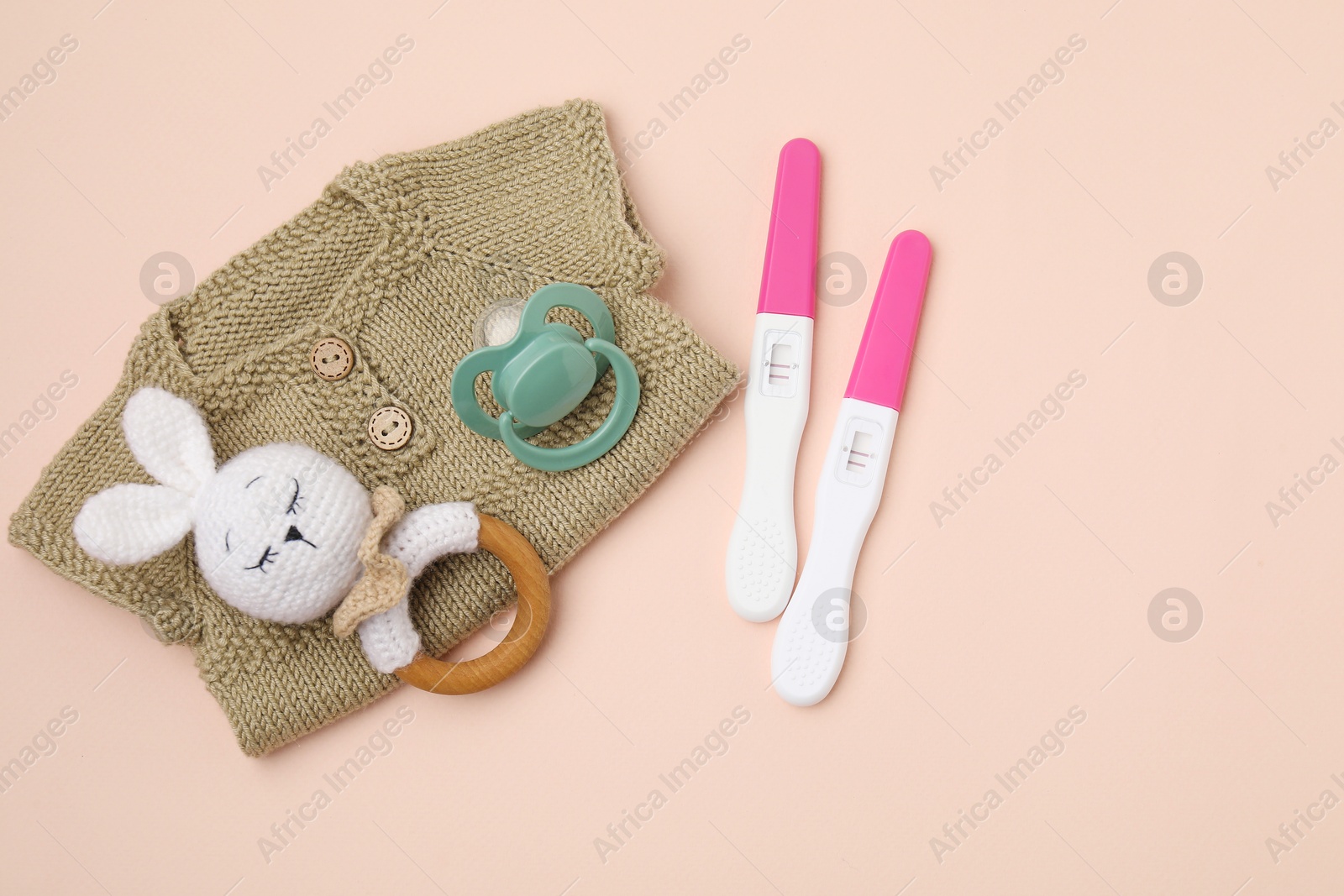 Photo of Pregnancy tests, rattle, baby clothes and pacifier on beige background, top view