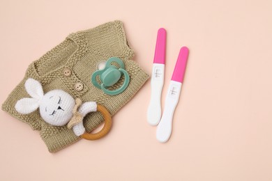 Photo of Pregnancy tests, rattle, baby clothes and pacifier on beige background, top view