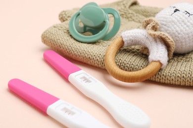 Photo of Pregnancy tests, rattle, baby clothes and pacifier on beige background, closeup