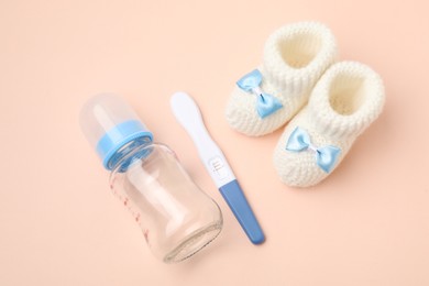 Photo of Pregnancy test, feeding bottle and baby booties on beige background, above view