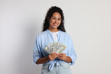 Happy woman with dollar banknotes on light grey background