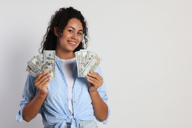 Happy woman with dollar banknotes on light grey background, space for text