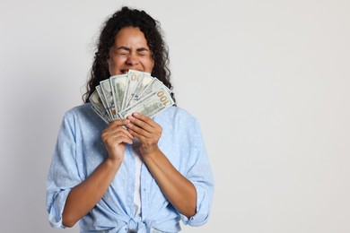 Happy woman with dollar banknotes on light grey background, space for text