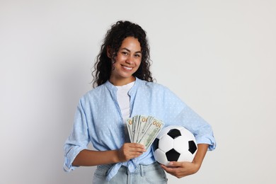 Happy woman with money and soccer ball on light grey background