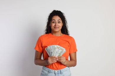 Smiling woman with dollar banknotes on light grey background