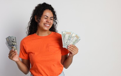 Happy woman with dollar banknotes on light grey background. Space for text