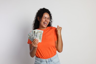 Happy woman with dollar banknotes on light grey background