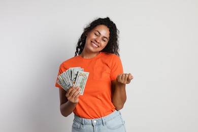 Happy woman with dollar banknotes on light grey background