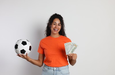 Happy woman with money and soccer ball on light grey background