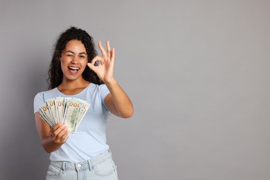 Photo of Happy woman with dollar banknotes showing ok gesture on grey background, space for text