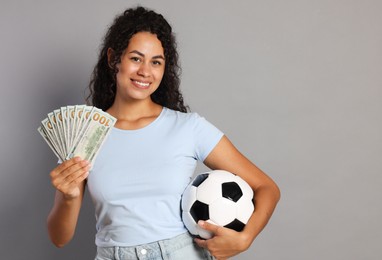 Happy woman with money and soccer ball on grey background