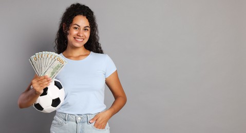 Happy woman with money and soccer ball on grey background, space for text