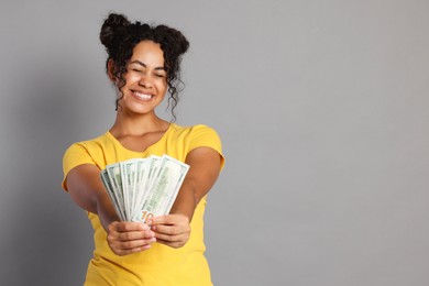 Happy woman with dollar banknotes on grey background, space for text