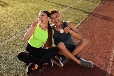 Happy winners with medals sitting at stadium on sunny day