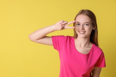 Photo of Teenage girl showing v-sign on yellow background