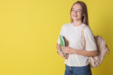 Teenage girl with books and backpack on yellow background, space for text