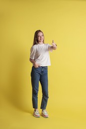 Teenage girl showing thumbs up on yellow background