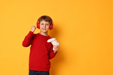 Photo of Happy little boy in headphones with controller on orange background. Space for text