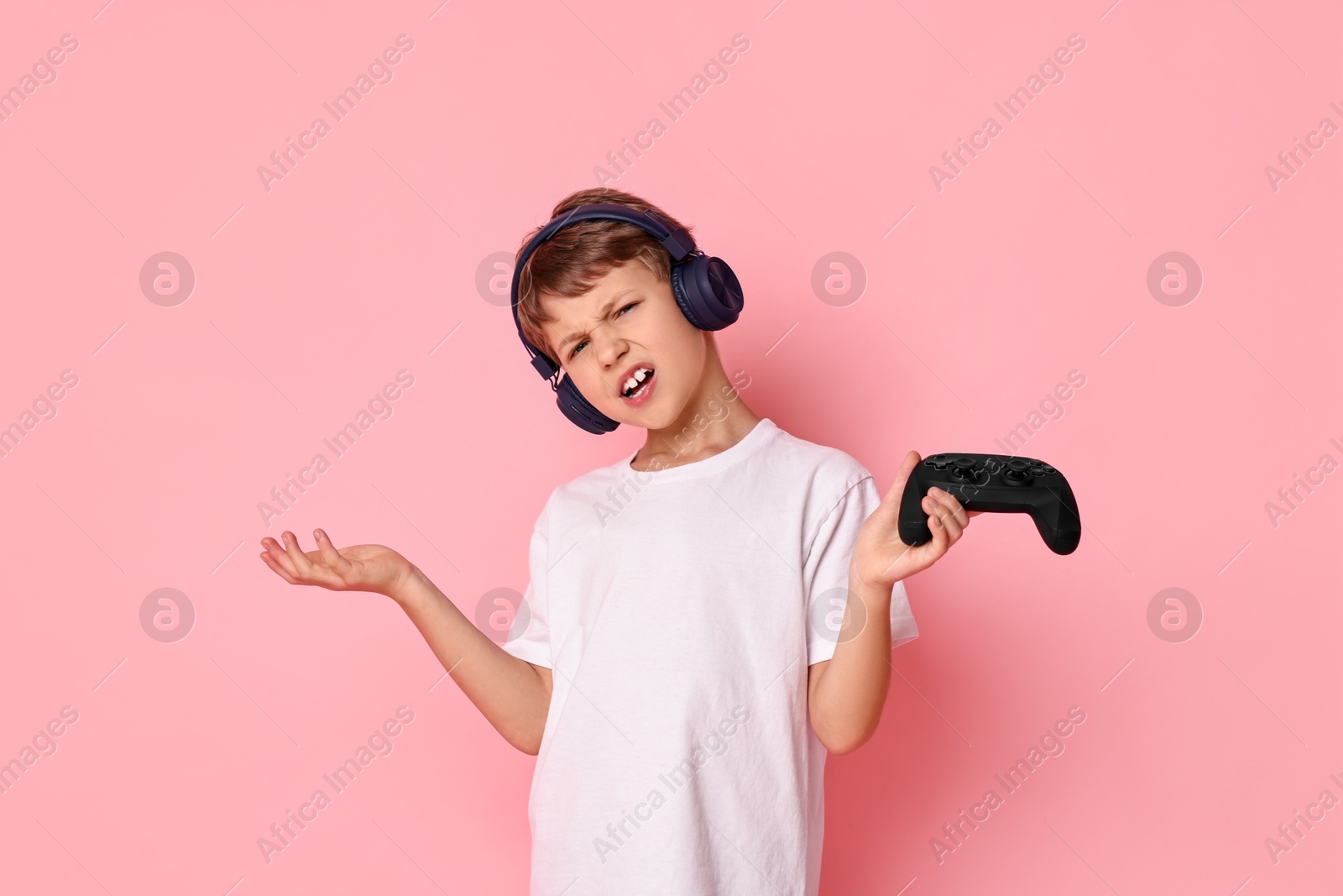 Photo of Cute little boy in headphones with controller on pink background