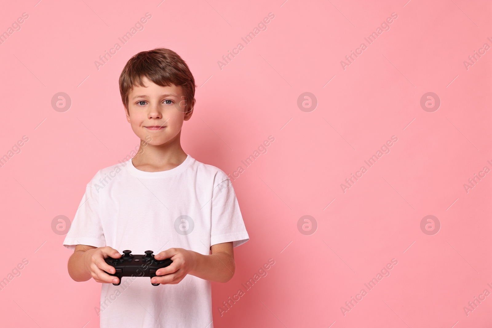 Photo of Happy little boy playing video game with controller on pink background. Space for text