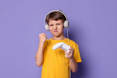 Cute little boy in headphones with controller on purple background