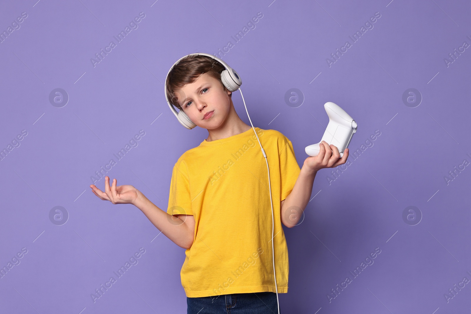 Photo of Cute little boy in headphones with controller on purple background