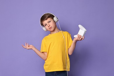 Cute little boy in headphones with controller on purple background