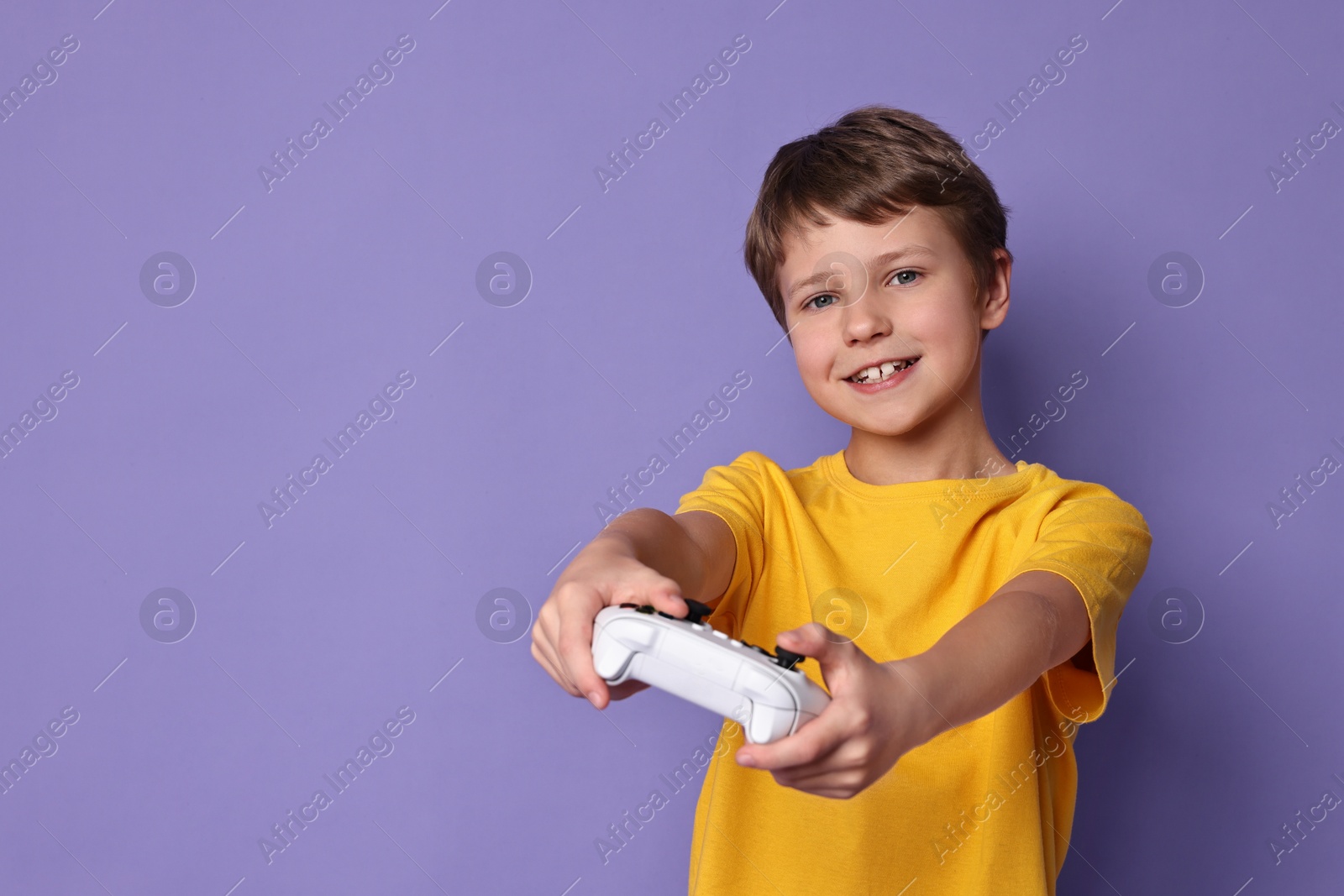 Photo of Happy little boy playing video game with controller on purple background. Space for text