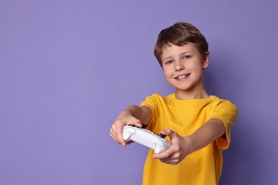 Happy little boy playing video game with controller on purple background. Space for text