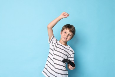 Happy little boy with controller on light blue background