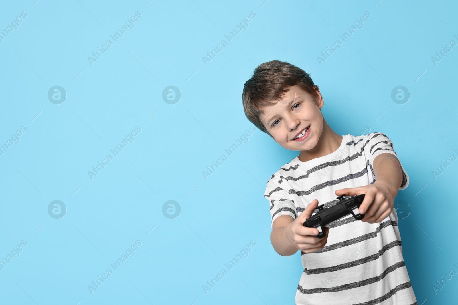 Photo of Happy little boy playing video game with controller on light blue background. Space for text