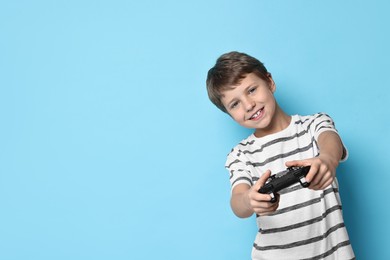 Happy little boy playing video game with controller on light blue background. Space for text