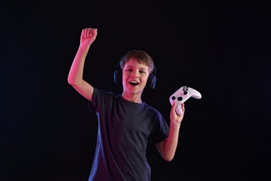 Photo of Happy little boy in headphones with controller on black background